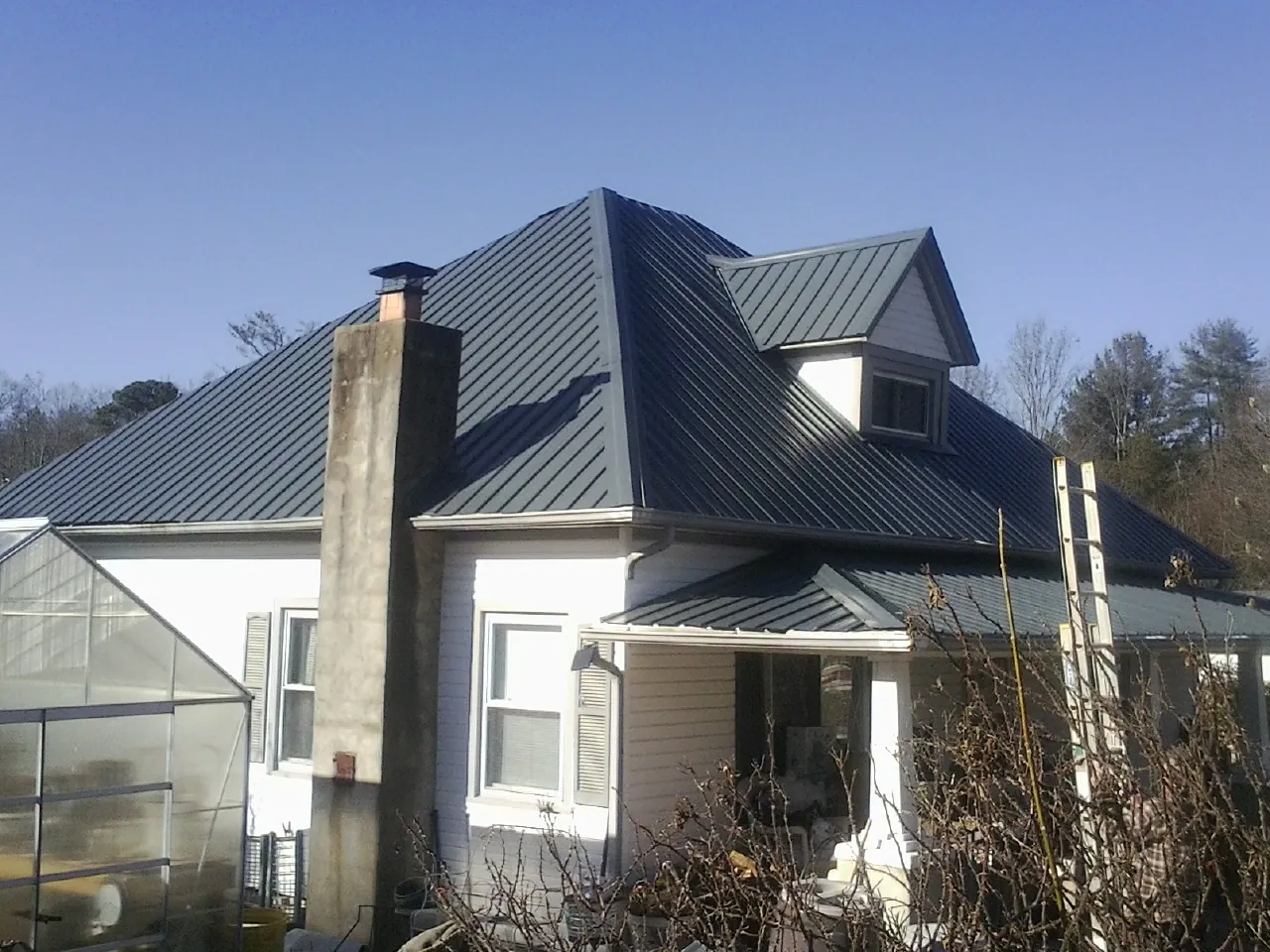 Dark blue standing seam metal roof on a white farmhouse with dormer — Slate & Tile Roof Repair by Roofing Brothers in Grayson
