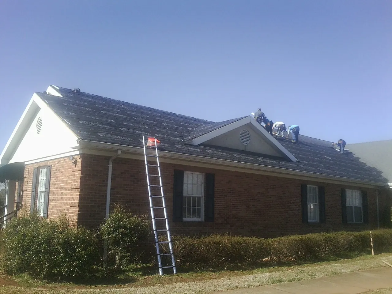 Crew tearing shingles off a brick ranch roof with a ladder set — Emergency Roof Repair work by our crew in Grayson