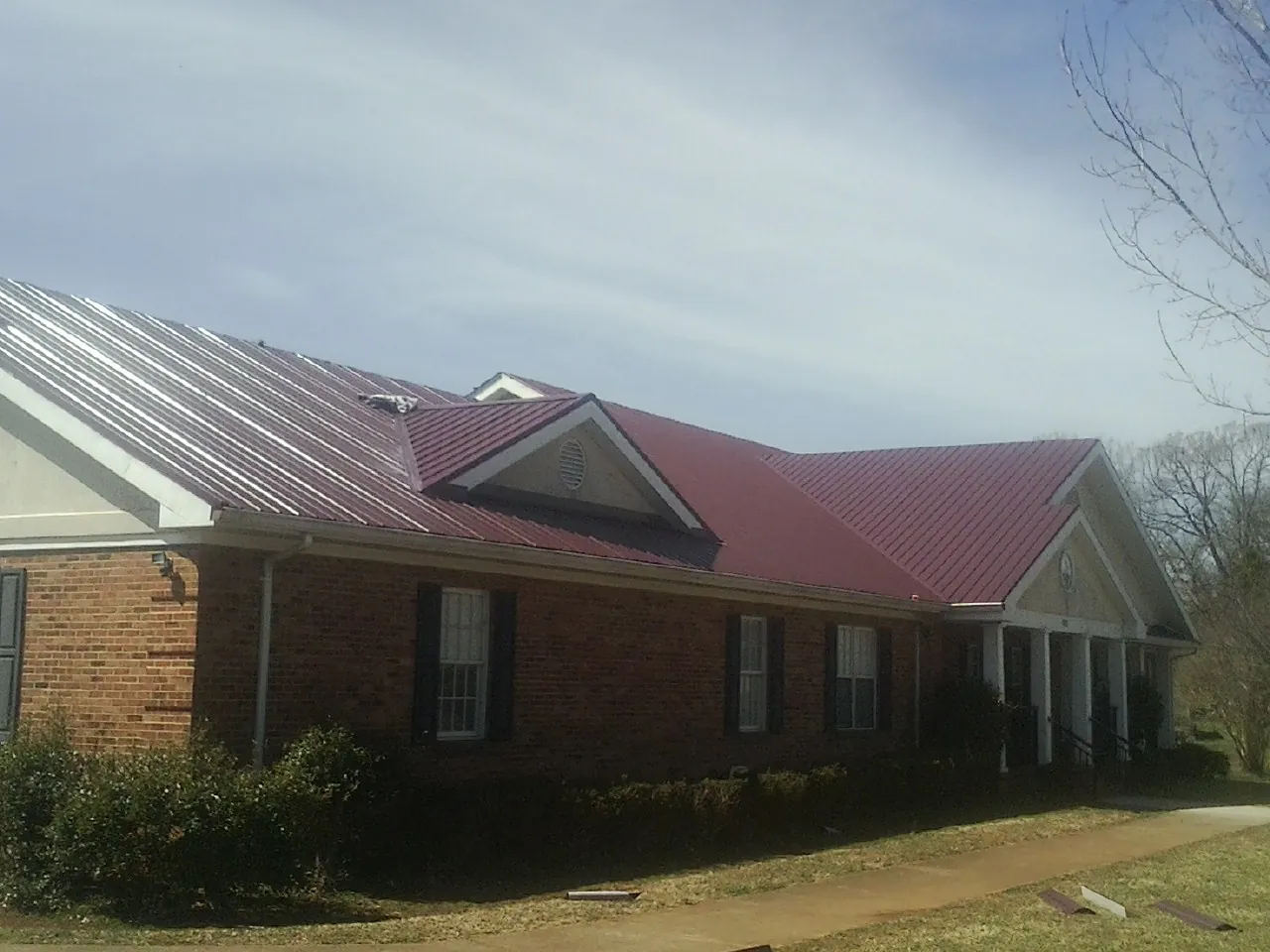 Red metal roof with gabled entries on a long brick building, from a Hail Damage Roof Repair job in Grayson