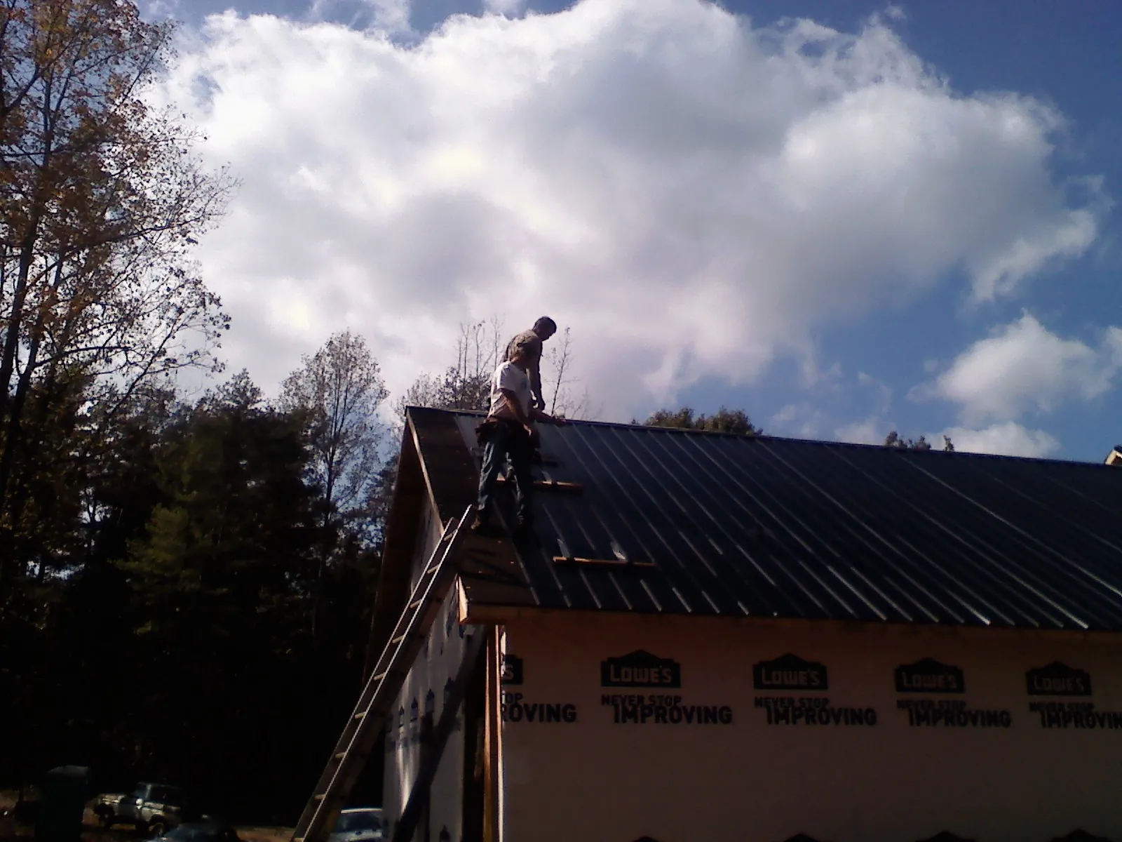 Roofer fastening dark metal panels high against a cloudy sky, from a Roof Inspection job in Grayson