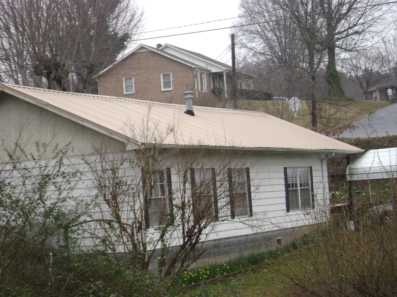 Tan metal roof on a white sided house set into a hillside — Commercial Roofing by Roofing Brothers in Grayson