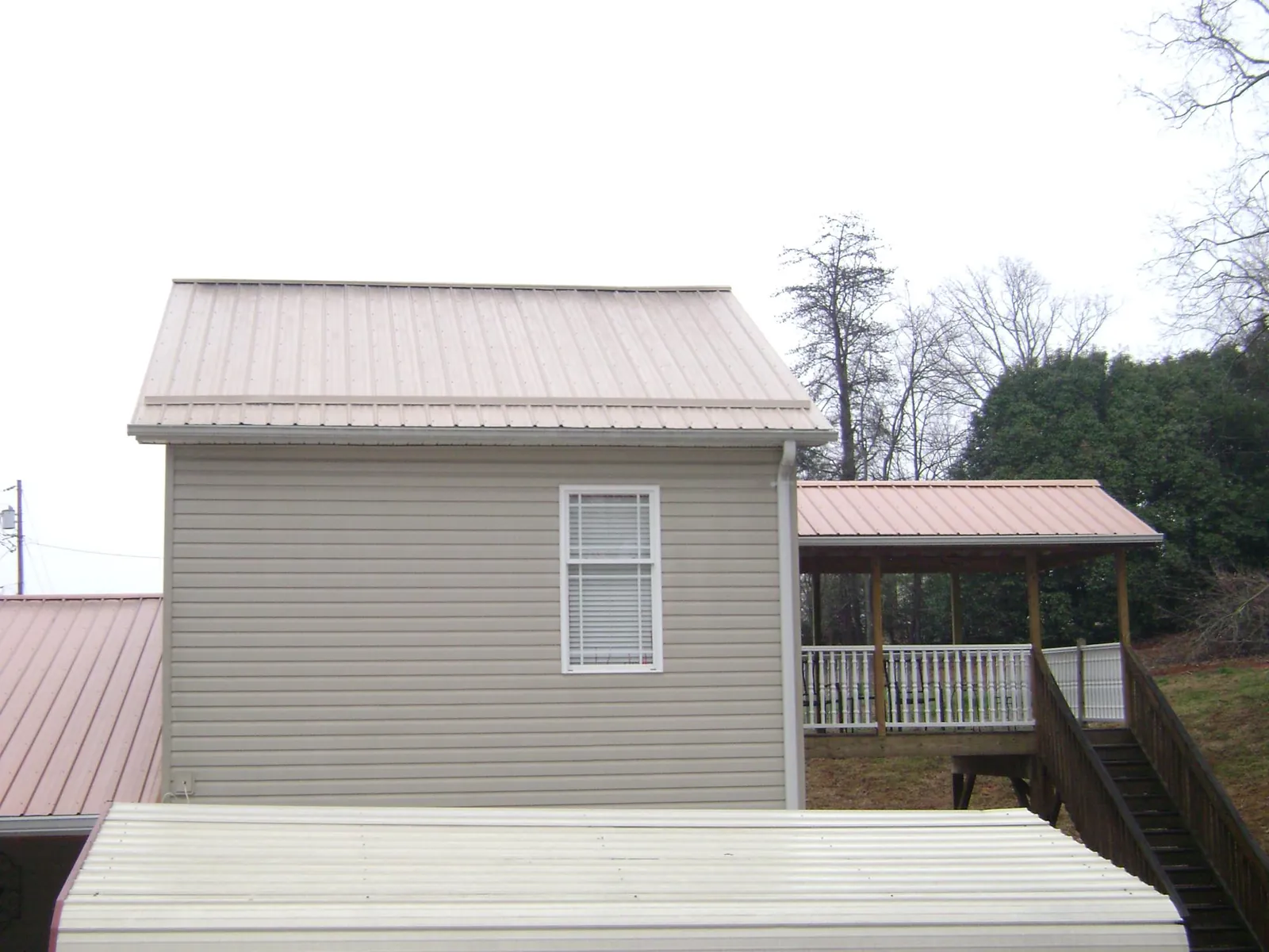 Tan metal roofs on a two story addition and attached porch, from a Roof Replacement job in Grayson